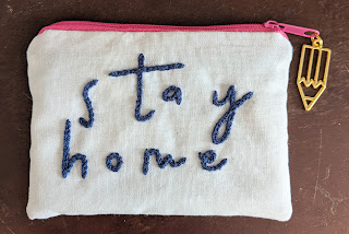 small zip purse with the words stay home embroidered on the front and a pencil charm on the zip