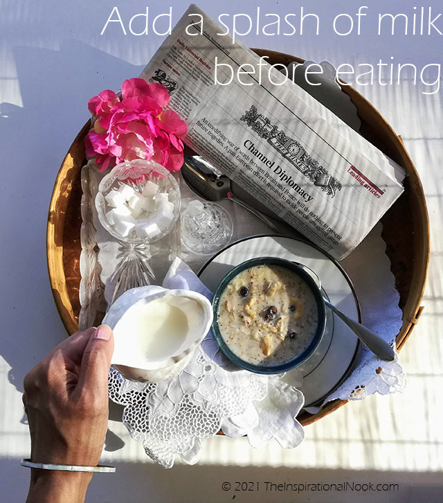 Girl pouring milk into a bowl of porridge on a tray, sugar cubes in a glass bowl, pink flowers on tray, lace tray cloth, newspaper on breakfast tray