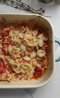 Foto di una teglia da forno con dentro dei pomodorini rossi e un panetto di formaggio feta, condito con origano olio e aglio