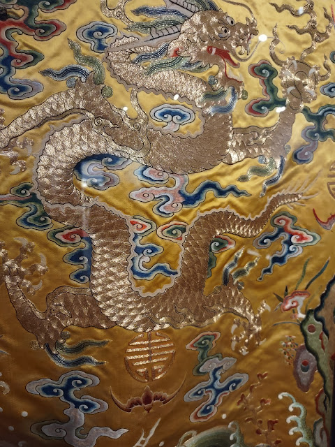 Photograph. Detail of a Chinese Emperor's dragon robe. Rich embroidery in multiple colors on a gold background.
