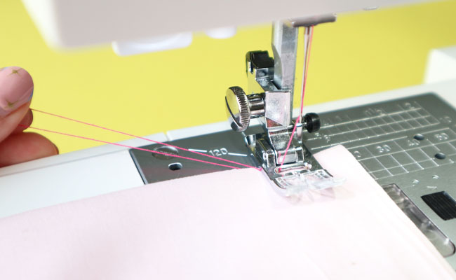 A hand holding the sewing machine threads whilst beginning to stitch