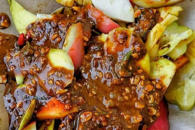 Colorful plate of Indonesian rujak buah with pineapple, cucumber, and green mango coated in spicy palm sugar sauce.