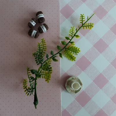 Two patterns of scrapbooking paper that looks like one-twelfth scale wallpaper with 4 balls of one-twelfth scale wool, a cup and saucer and a length of plastic fake plant.