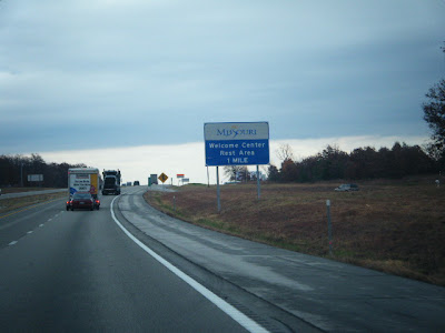 The view from my van on moving day:  It's overcast, the Missouri welcome sign is on the side of the road, and ahead is a 26-foot U-Haul towing our little red car