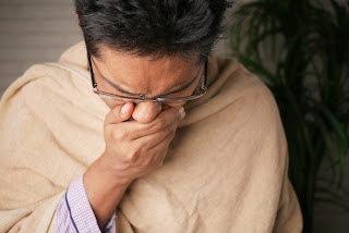 a person holding their mouth, wrapped up in a blanket