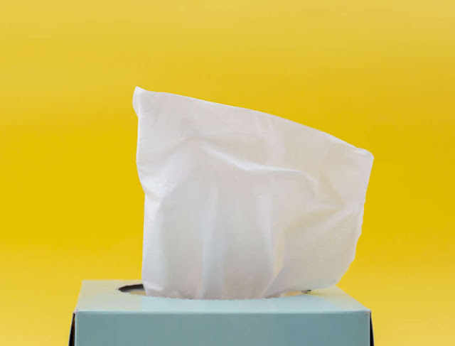 a white paper tissue sticking out of a blue box of tissues with a bright yellow background