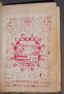 An elaborately decorated title page. The designs and letters are cut out of the page and show the red silk set behind it.