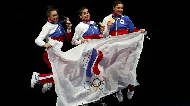Três atletas russas seguram a bandeira do Comitê Olímpico Russo e pulam comemorando a vitória