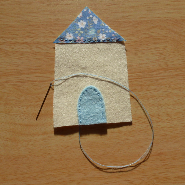 Blue fabric and felt detail being hand sewn onto a felt house