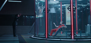 Scene with Jen Walters, a mousy woman in a business suit, speaking with Emil Blonsky, an older white man in a prison jumpsuit. He's in a high tech prison cell with clear walls.