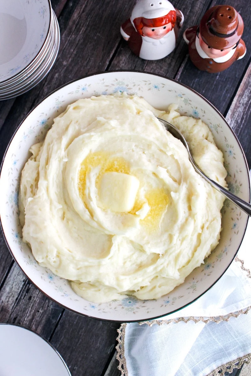 Top view of mashed potatoes in a white bowl with smal blue flowers on a wood background.