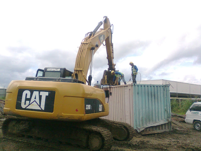 Tying the sling from the container van to the arm of the backhoe