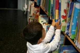 A small child reaching for books on a shelf