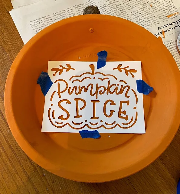 Photo of an orange pie tin with a stencil on top.