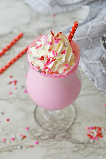 pink milkshake in a clear glass with a red straw.
