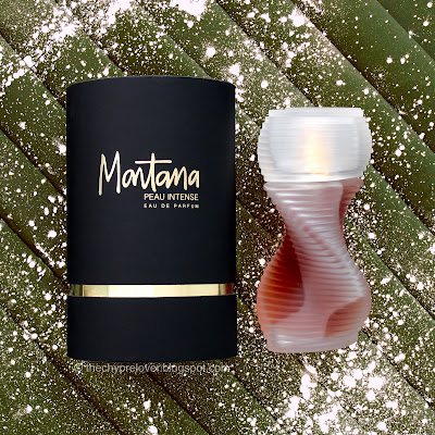 The black cilindrical bottle and helicoid bottle of Peau Intense by Montana lying flat on a dark green, pleated material sprinkled with white powder