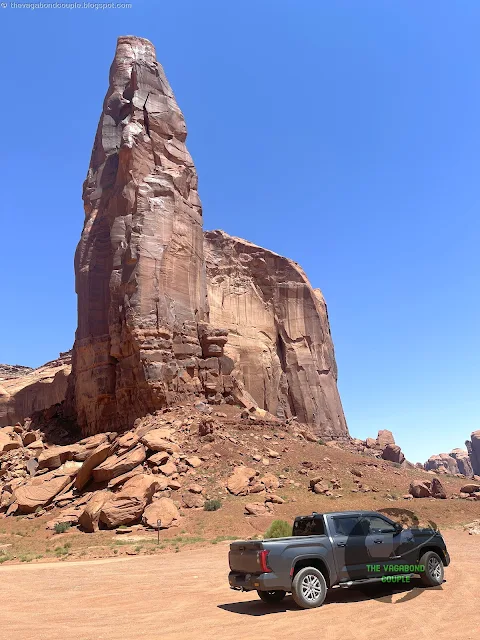 Raingod Mesa standing tall under a vast blue sky, surrounded by the golden desert of Monument Valley