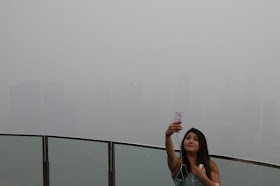 A woman takes a selfie with the skyline of the central business district shrouded by haze in Singapore on 14 September 2015.