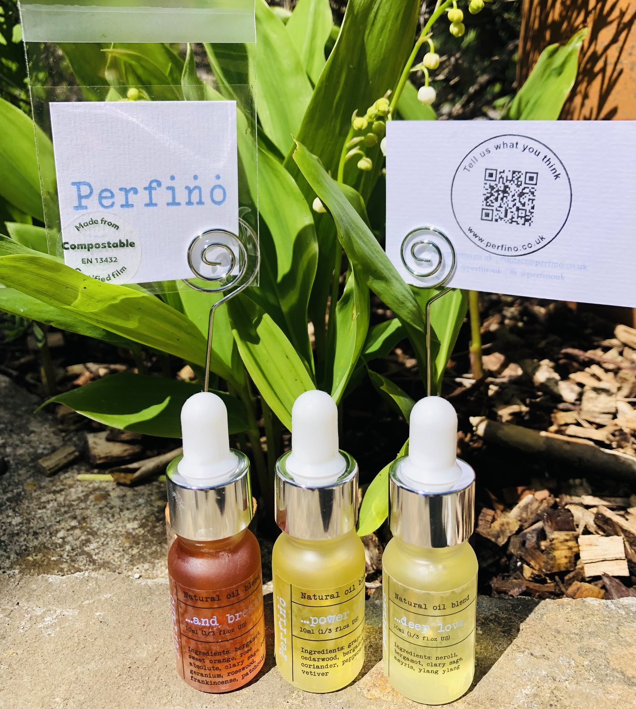 three bottles of natural essential oil blends from Perfino all lined up on the ground in front of plants