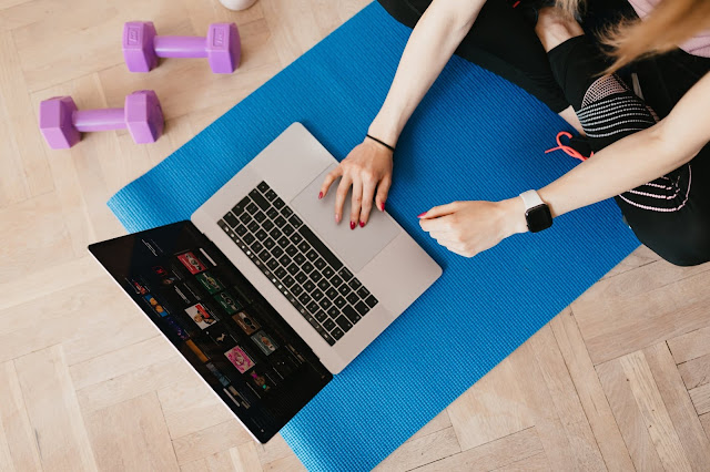 A girl using a laptop while sitting on a yoga mat with weights next to it