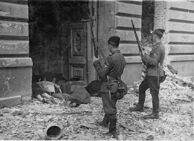 Two Ukrainian Askaris peer into a doorway past the bodies of Jews killed during the suppression of the Warsaw Ghetto Uprising, 1943.