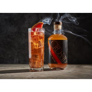 bottle_of_crossip_non_alchoholic_spirit_named_dandy_smoke_pictured_alongside_a_tall_full_glass_tumbler_with_a_black_background_to_highlight_smoke_special_effects