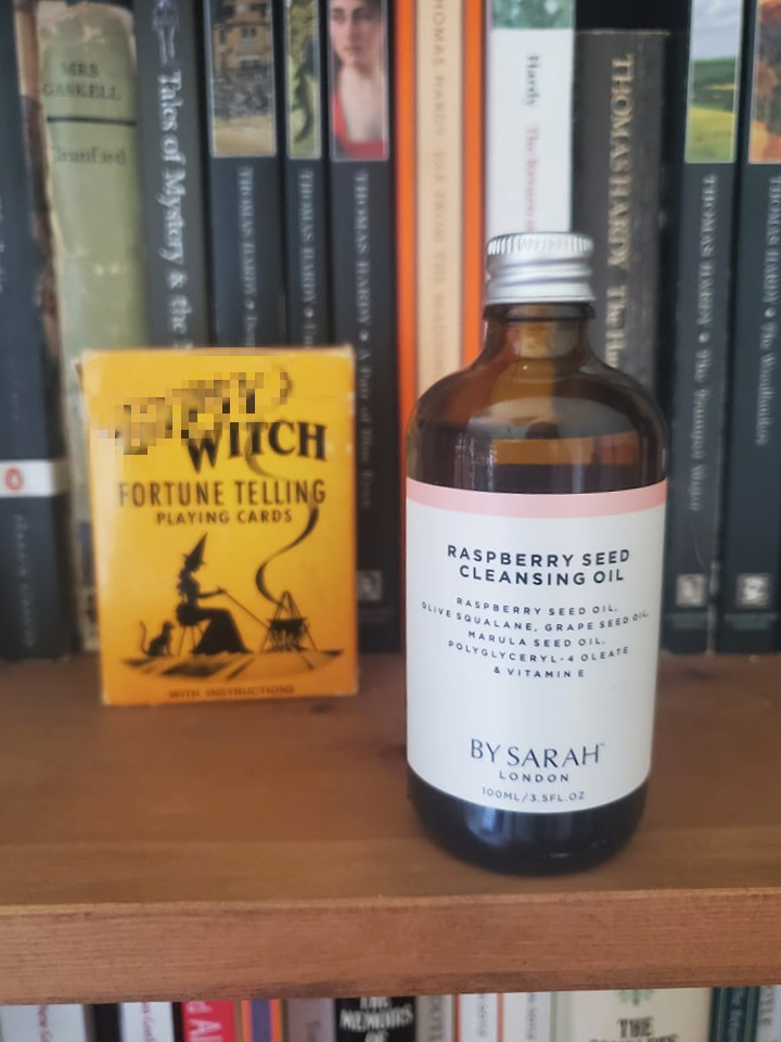 Raspberry Seed Cleansing Oil from By Sarah London on a bookshelf surrounded by books and a vintage deck of playing cards