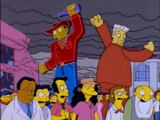 Gif from The Simpsons Treehouse of Horror VI segment "Attack of the 50ft Eyesores" - the gawking crowd full ignoring the rampaging giant advertisement figures, they fall to the ground: a neon cowboy, a giant Kent Brockman, and a Devil