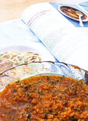 Sundried tomato pesto in a glass bowl next to an open cook book