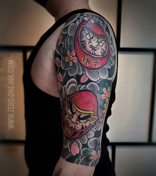 man in standing position showing a red daruma doll with Japanese black and gray clouds and pink cherries blossom done by Horipeppe mukade at zero one ink tattoo in Sacramento California