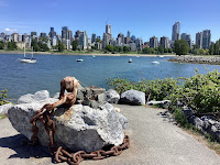 Photo by Sheila Webber of a rock with chain from a ship and a view across the water to downtown Vancouver in May 2024