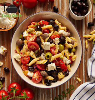Close-up of a spoonful of Mediterranean pasta salad with olives, tomatoes, and feta, on a wooden table.