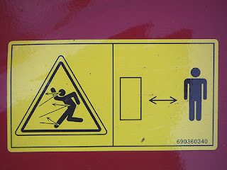 Photo by Deirdre: a safety decal showing lines rebounding from the front of a human figure, and another human figure linked to a large empty box by two-way arrows