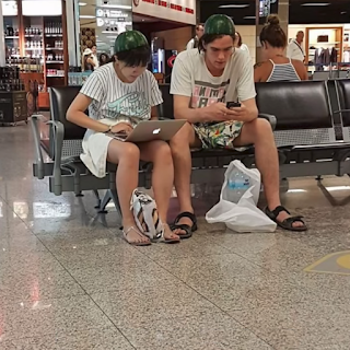 Couple at airport, wearing watermelon halves on their heads