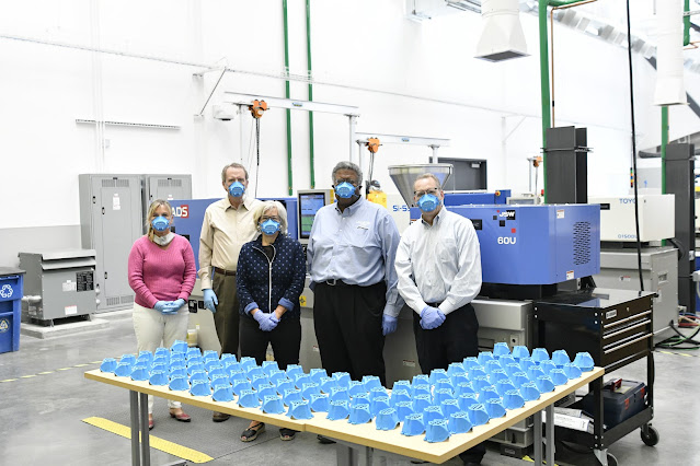 SLCC President Deneece G. Huftalin and cabinet members with dozens of masks produced by the injection molding machine behind them.