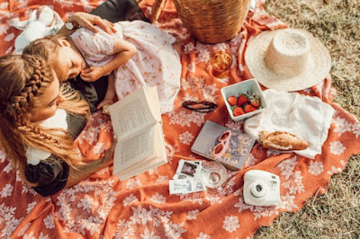 Mother and daughter are lying on an orange picnic blanket and reading