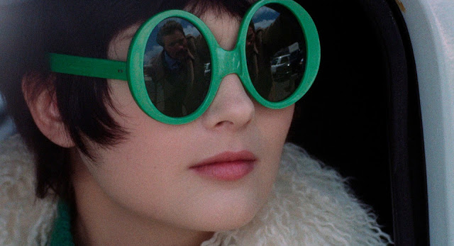 Pamela Tiffin in close-up wearing very large round green-rimmed sunglasses.