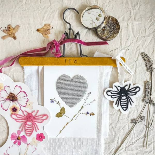 stitched heart on paper held by trouser hanger surrounded by floral wreath, pins, dried flowers
