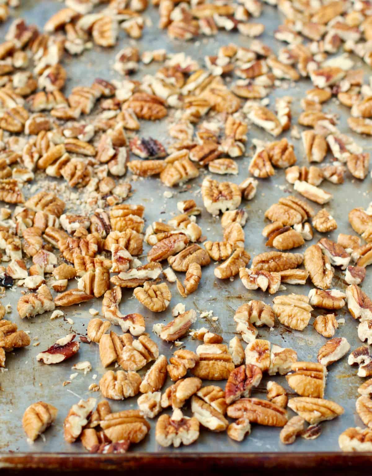 Pecan pieces on a rimmed baking sheet.