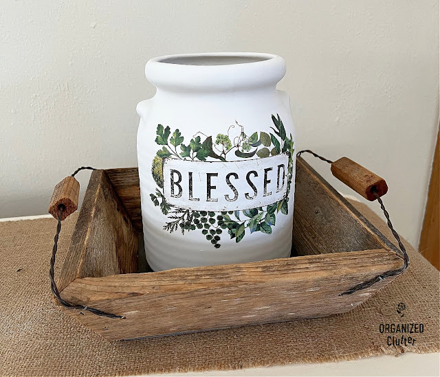 Photo of an upcycled crock with spray paint & decor transfer displayed in a barn wood basket.
