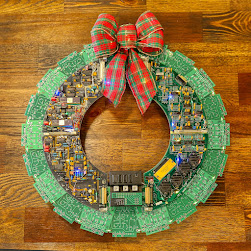 A wreath made from computer parts, It has a red & green plaid ribbon at the top. Photo by Mick Haupt on Unsplash.