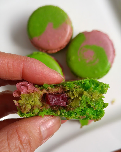 A cross section of a raspberry matcha macaron where the raspberry jelly is clearly seen.