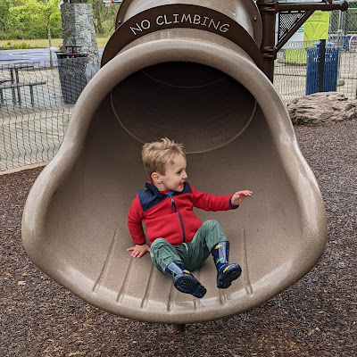 Toddler boy emerging, elated, from the bottom of a twisty slide.
