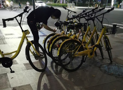 A girl scans the QR code at a street corner in Shenzhen to unlock a bike ride. Bike sharing is popular in China, with bicycles from bike sharing companies lining streets. Each company has its bikes in a different colour. The yellow ones are from Ofo.