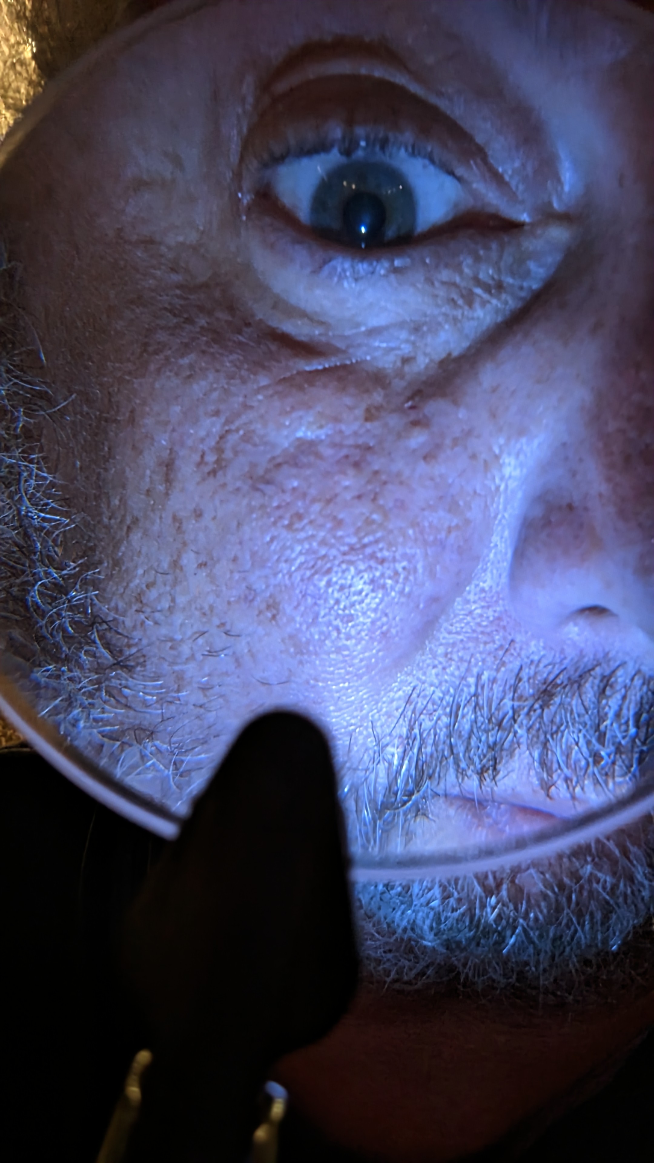 Close-up selfie of a man looking through a magnifying glass.