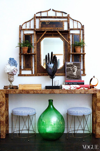 Side table in Rebecca de Ravenel's dining room with two metal stools with blue and white seats, a large glass bottle and faux bamboo mirror