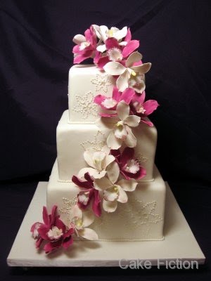 A three tier wedding cake decorated with cascading magenta and white 