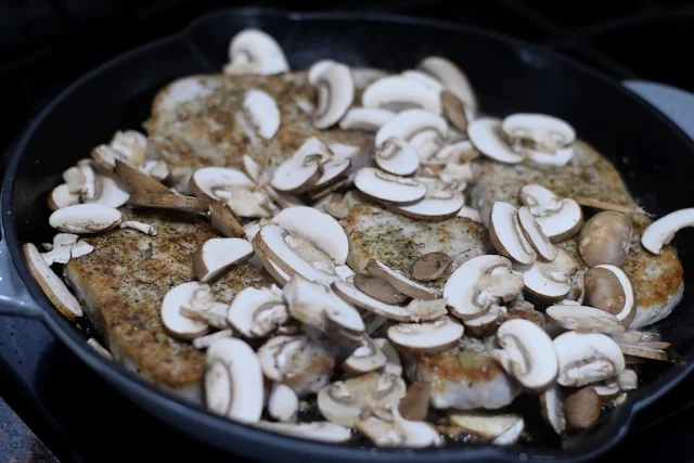 The sliced mushrooms in the pan with the browned pork chops. 