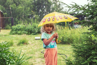 Young blonde girl holding an umbrella while standing in a garden.