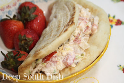 A chicken salad mixed with shredded lettuce, sliced green onion, chopped tomato, shredded cheese, chopped pecan and dressed with mayonnaise, pictured stuffed in a toasted pita.